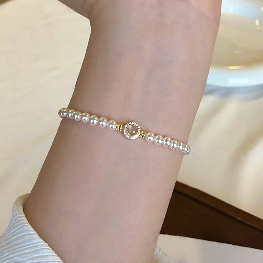Klassisches Tessa's Schimmerndes Halo-Perlenarmband aus glänzenden Kunstperlen mit einem goldfarbenen Zirkonia-Mittelstück auf einem weißen Teller