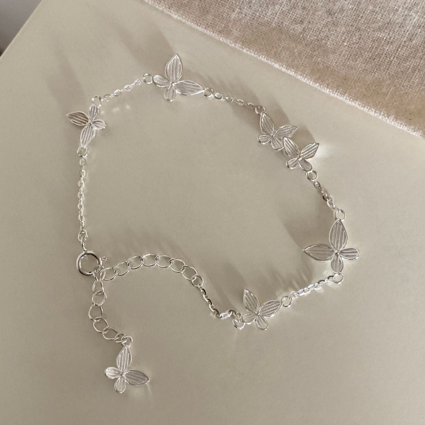 Versilbertes Armband mit gravierten Schmetterlingsblättern auf weißem Hintergrund.