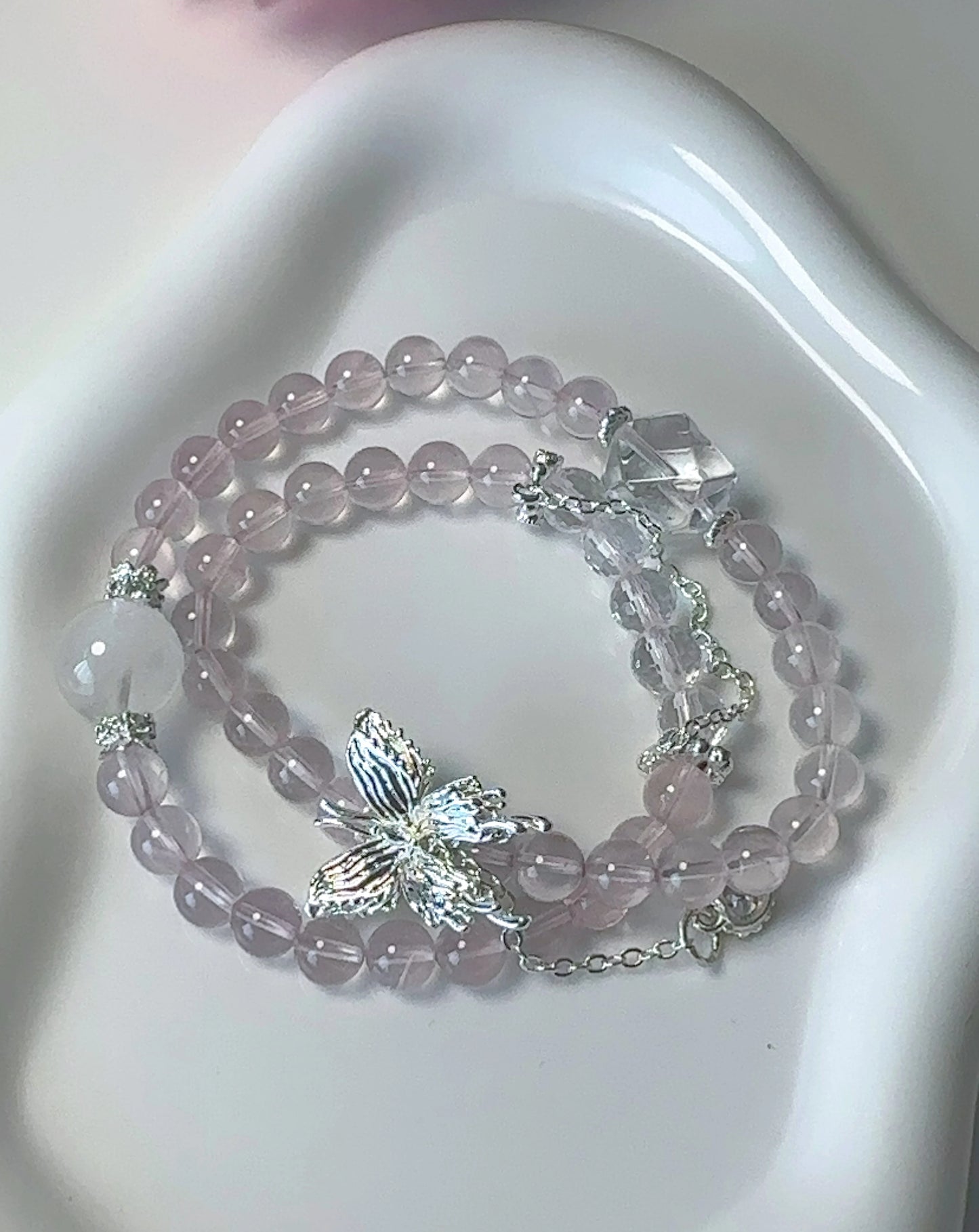 Rosa Rosenquarz-Perlenarmband mit Schmetterlingsanhänger – doppelt um den Finger gewickelt.