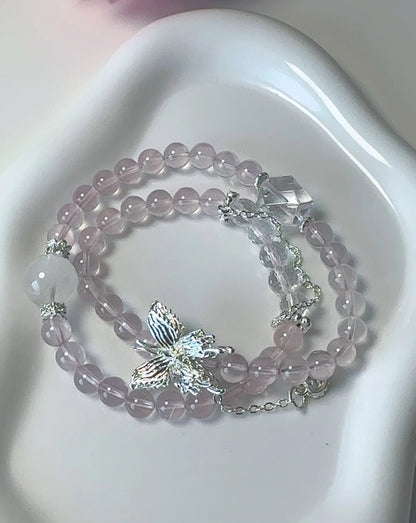 Rosa Rosenquarz-Perlenarmband mit Schmetterlingsanhänger – doppelt um den Finger gewickelt.