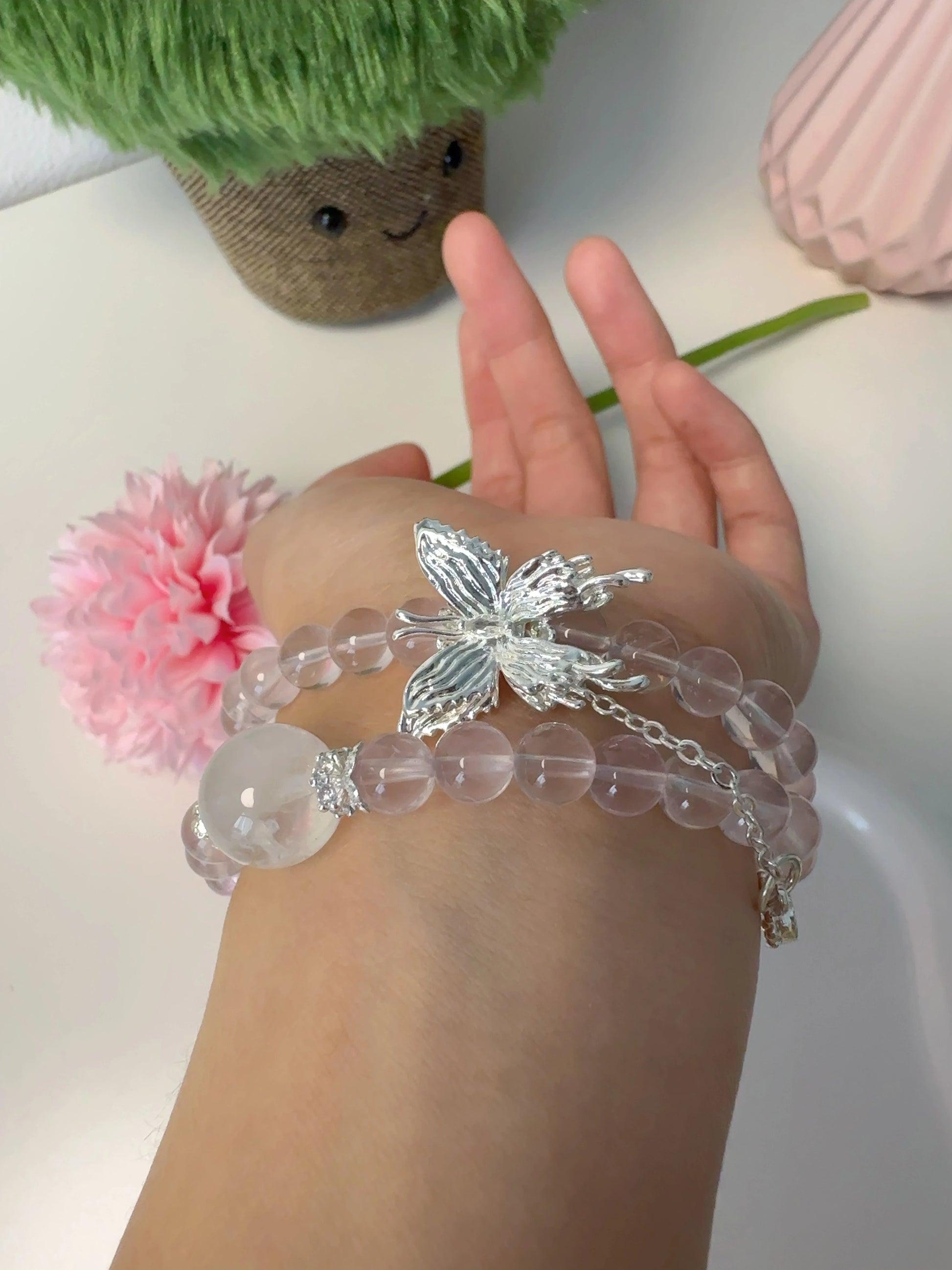 Rosa Rosenquarz-Perlenarmband mit Schmetterlingsanhänger – doppelt um den Finger gewickelt.