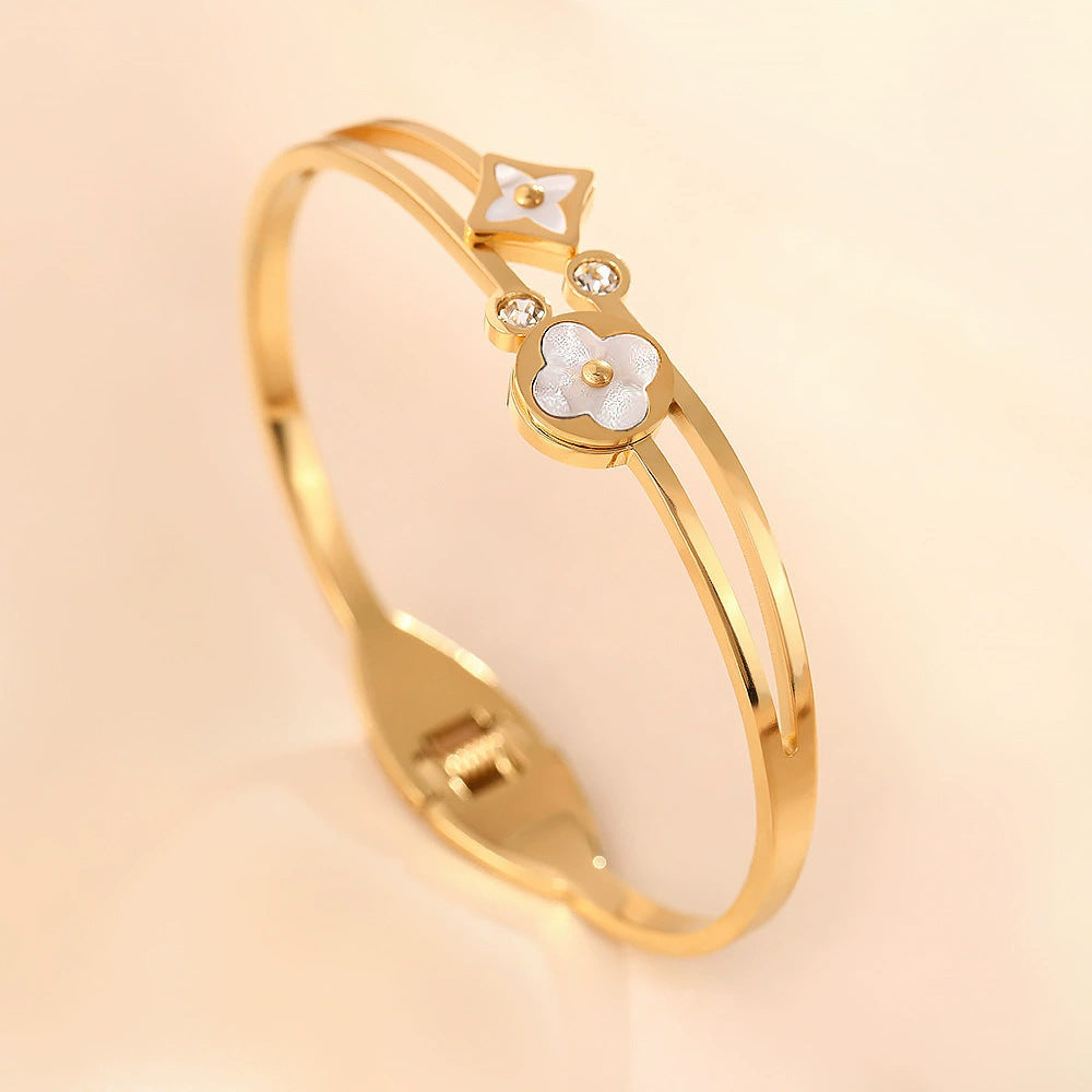 Vergoldeter Armreif mit weißen Perlmutt-Blumen und Zirkonia auf weißem Hintergrund