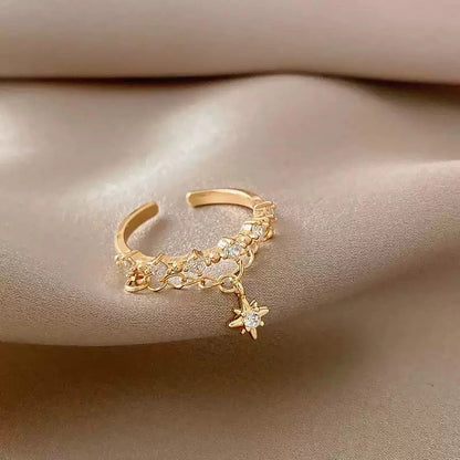 Vergoldeter Doppelring mit Sternanhänger und Kettenelement, auf Seidenstoff liegend.