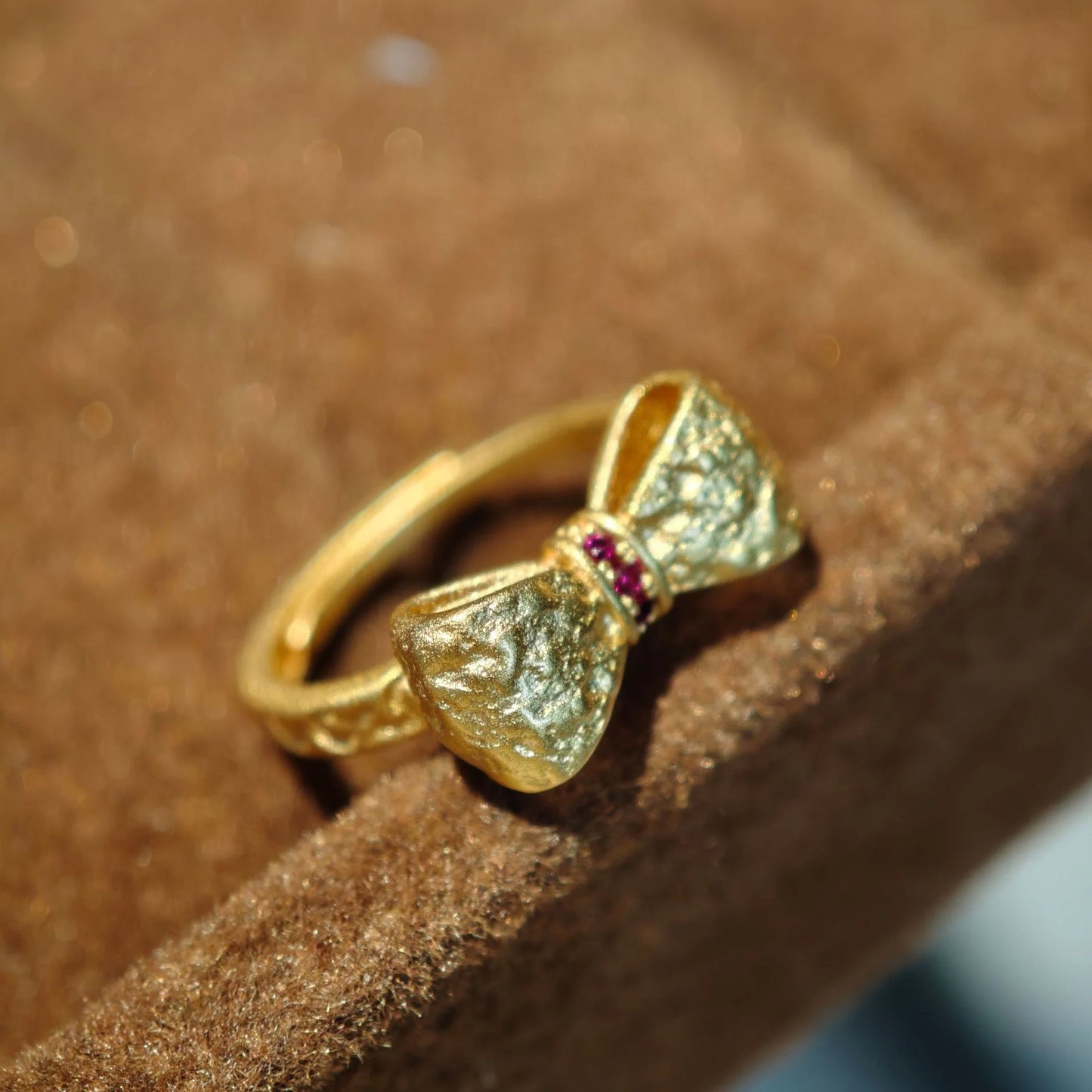 Goldener Ring in Schleifenform mit texturierter Oberfläche und roten Steinen