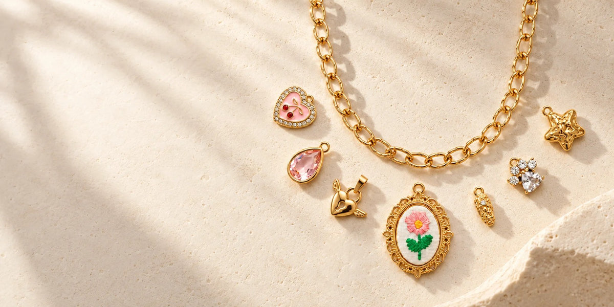 Goldfarbene Gliederkette mit verschiedenen Charms auf hellem Stein