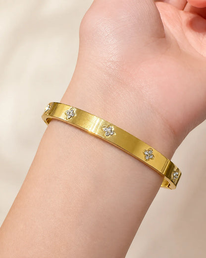 Gold-tone cubic zirconia clover bangle with small floral motifs, in a close view on the inside of the wrist.