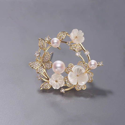 Elegante goldene Blumenkranz-Brosche mit Zirkoniablättern, geschnitzten Muschelblüten und rosa Süßwasserperlen – ideal für festliche Anlässe oder als Geschenk