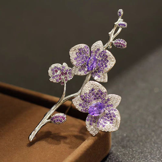 Elegante Orchideen-Brosche mit lila Zirkonia und Blütenmotiv auf silbernem Zweig