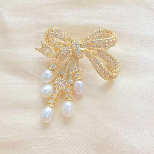 Goldene Schleifen-Brosche mit schimmernden Zirkonia und herabhängenden Süßwasserperlen – elegantes Design für festliche Anlässe